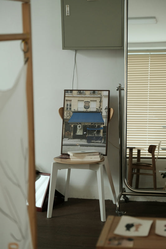 A framed parisian scene sits on a chair.