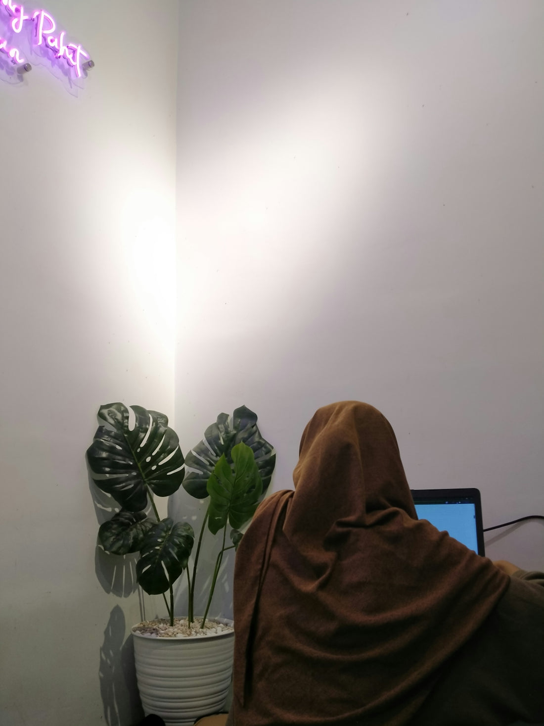 Woman in hijab working on laptop near plants